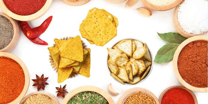 Different types of crackers in bowls surrounded by bowls of spices
