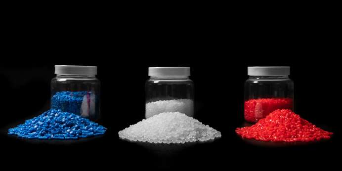 Blue, white, and red plastic pellets stored in jars with pellets piled in front