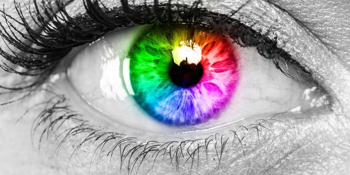 Close-up of a human eye in black and white with the iris in full rainbow color.