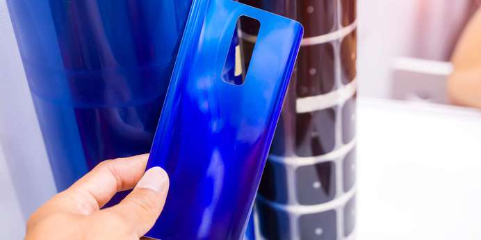 Hand holding a blue piece of plastic with additional opaque plastic in the background